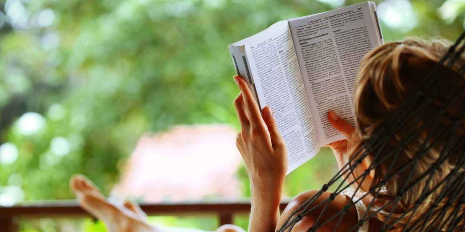 Frau entspannt in einer Hängematte und liest ein Buch – Inspiration für Tipps zum Stressabbau und einen stressfreien Alltag.