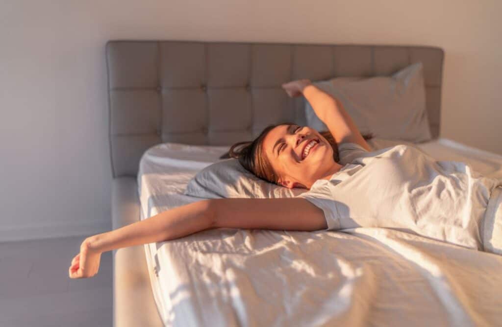 Frau, die entspannt und lächelnd im Bett liegt.