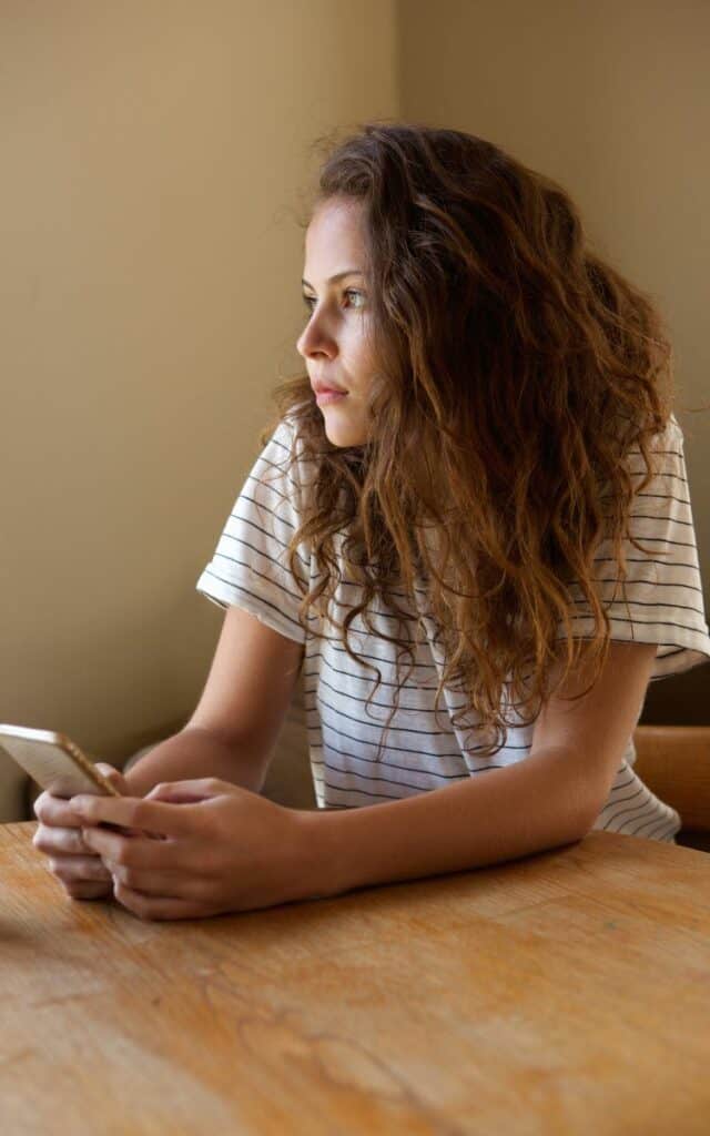 Nachdenkliche Frau mit Smartphone, als Symbol für die Herausforderung der digitalen Balance.