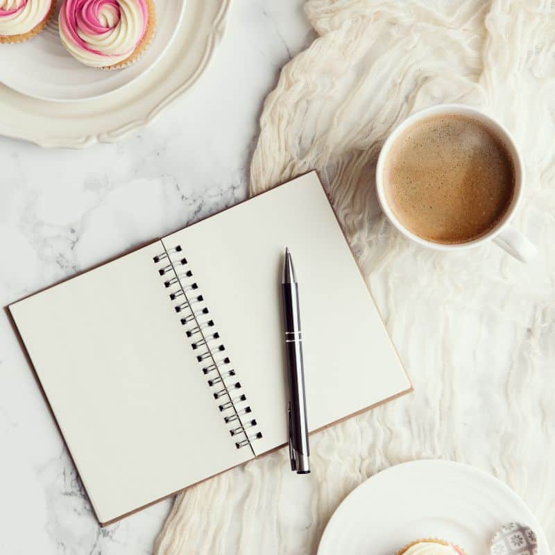 Offenes Notizbuch mit Kugelschreiber, Kaffee und Cupcakes auf Marmortisch – Inspiration für achtsames Schreiben mit den Soulnotes.
