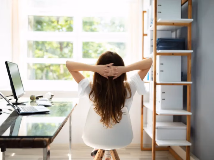 Frau sitzt entspannt am Schreibtisch mit Blick nach draußen und stärkt ihre Resilienz im Berufsleben durch bewusste Pausen.