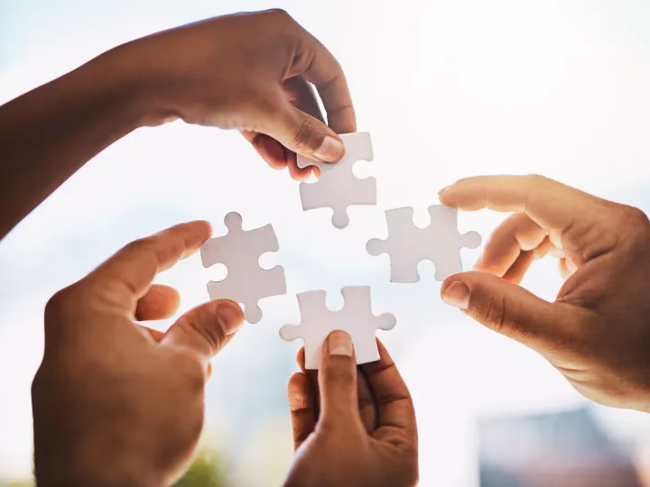 Vier Hände halten Puzzleteile zusammen, symbolisieren Teamwork und Resilienz im Berufsleben.