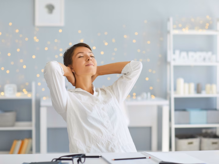 Frau lehnt sich entspannt zurück am Schreibtisch, genießt eine kurze Pause zur Stärkung ihrer Resilienz im Berufsleben.
